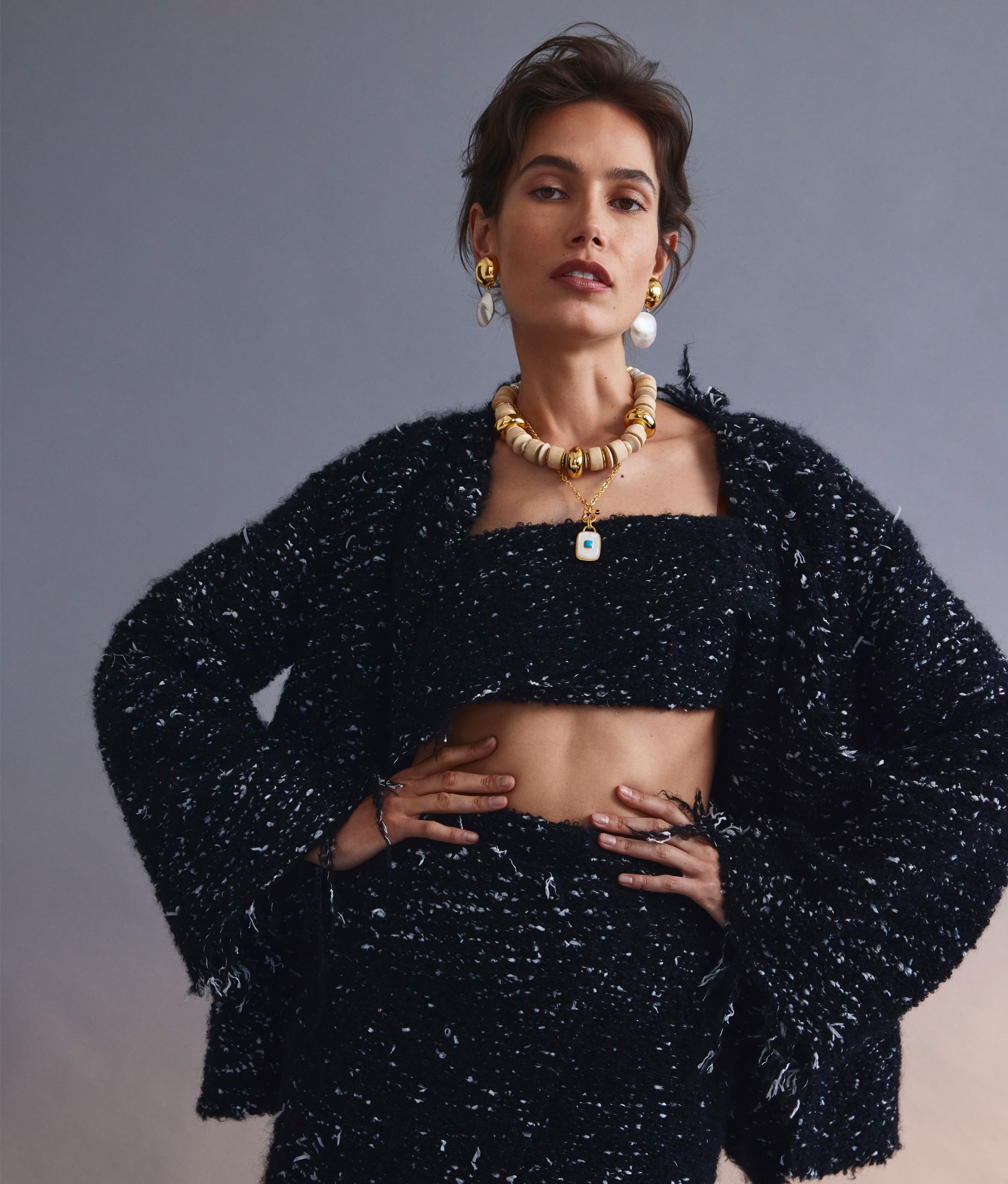 Model on grey backdrop wears black textured outfit with Ancient City Necklace, Interval Collar, and Rodan Pearl Earrings