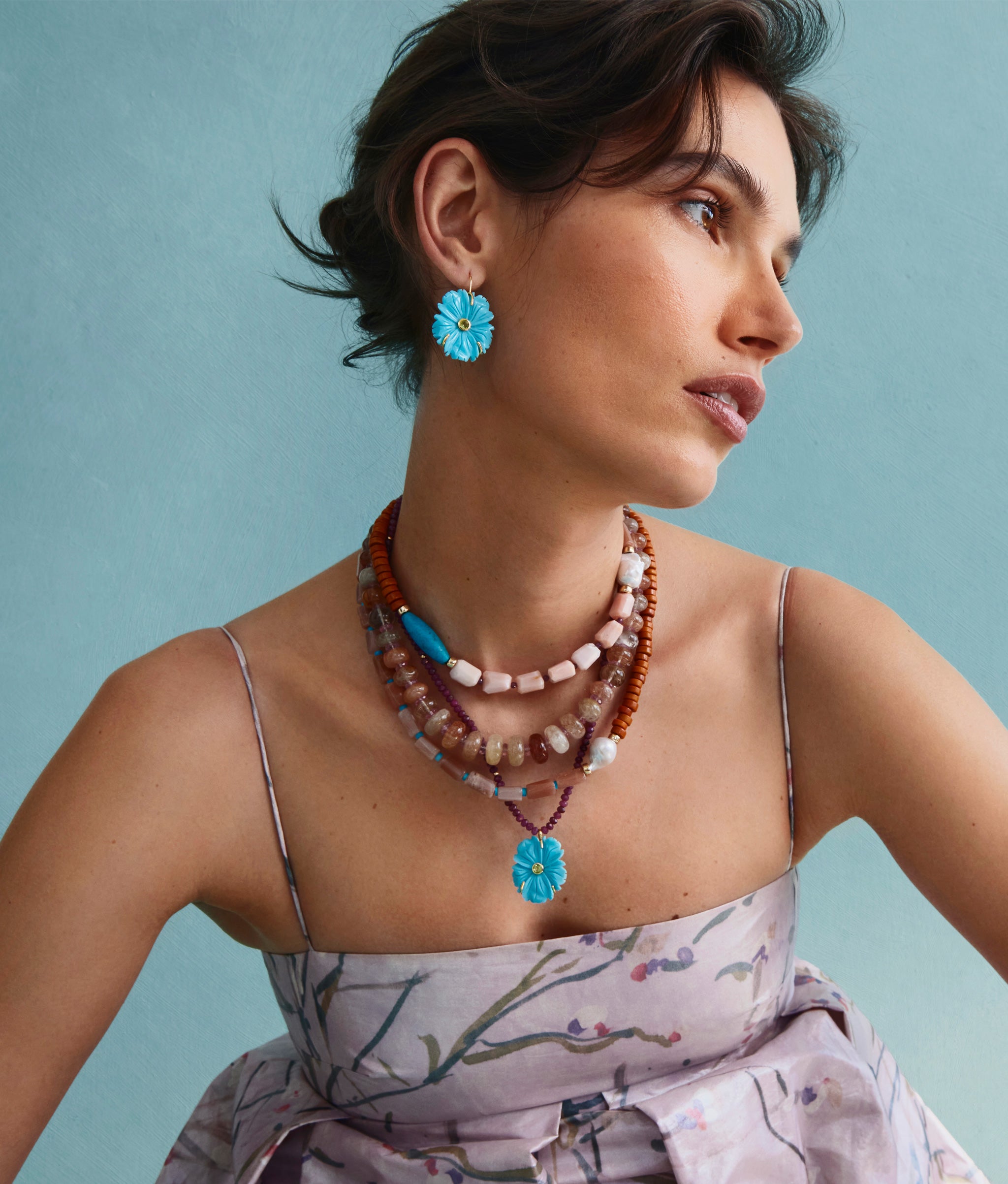 Model on blue backdrop wears floral dress with assorted jewelry including Cabana Necklace in Savannah.