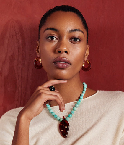 Model on woodgrain backdrop wears cream sweater with Organic Hoops and Vinca Leaf Necklace