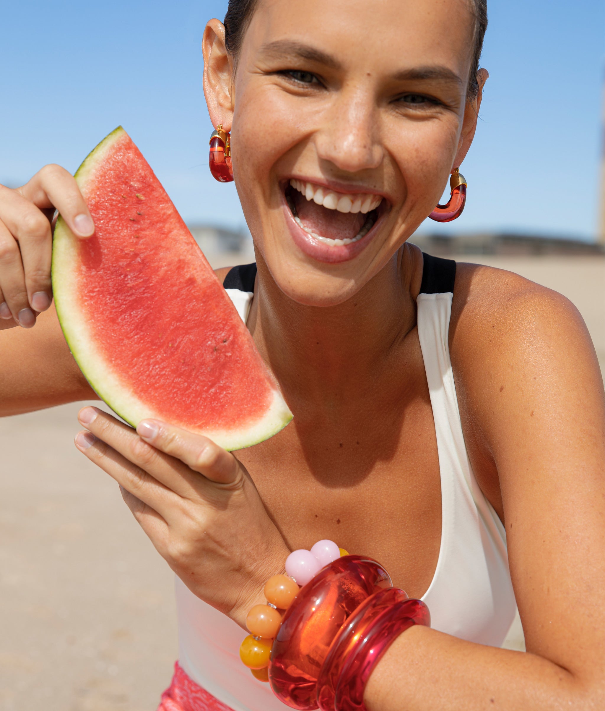 Model with watermelon wearing Organic Hoops in Persimmon paired with Arc Cuff, Ridge Cuff, and Olympia Bracelet.