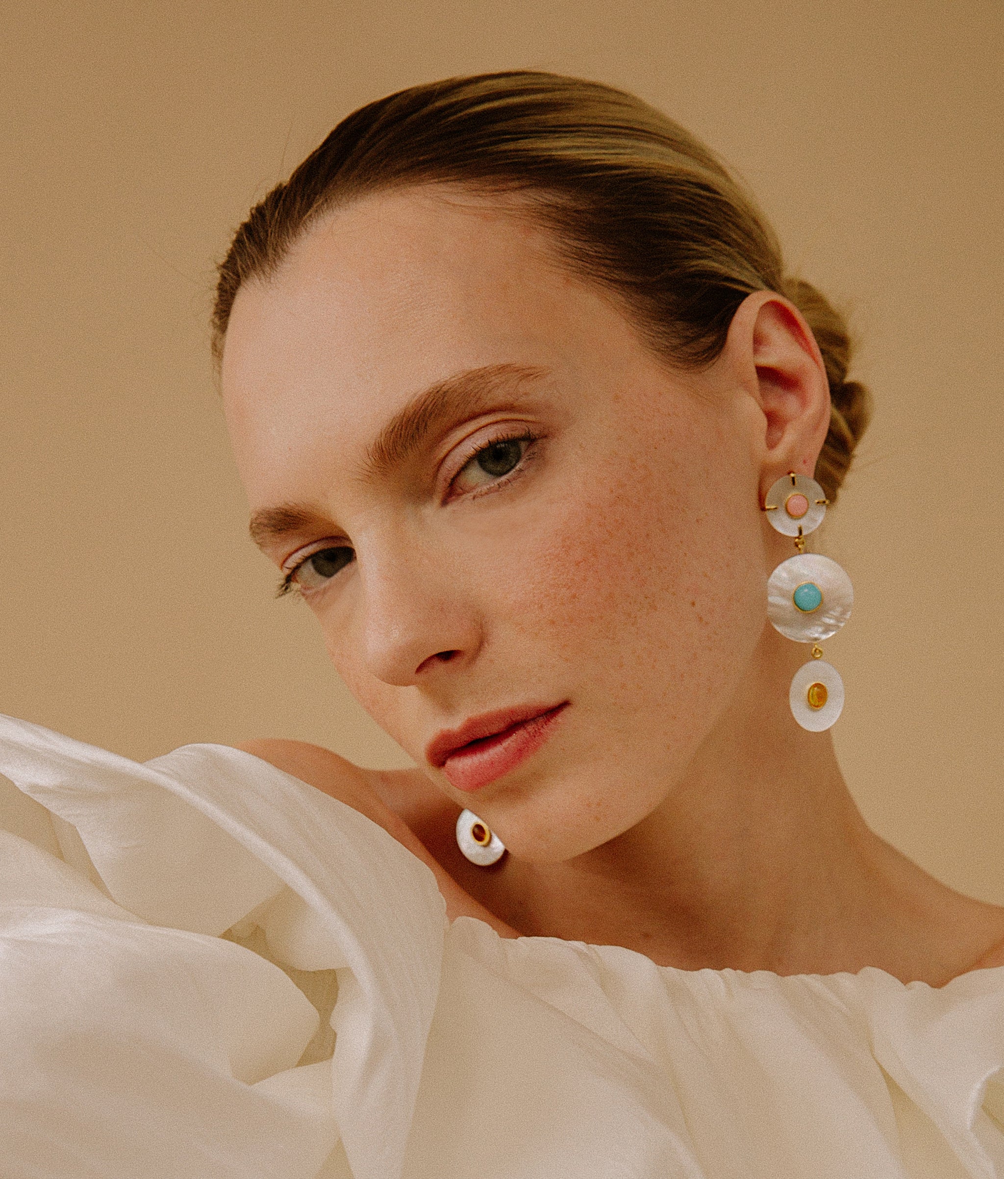 Close-up of model on tan background wearing Tropic Pearl Earrings.