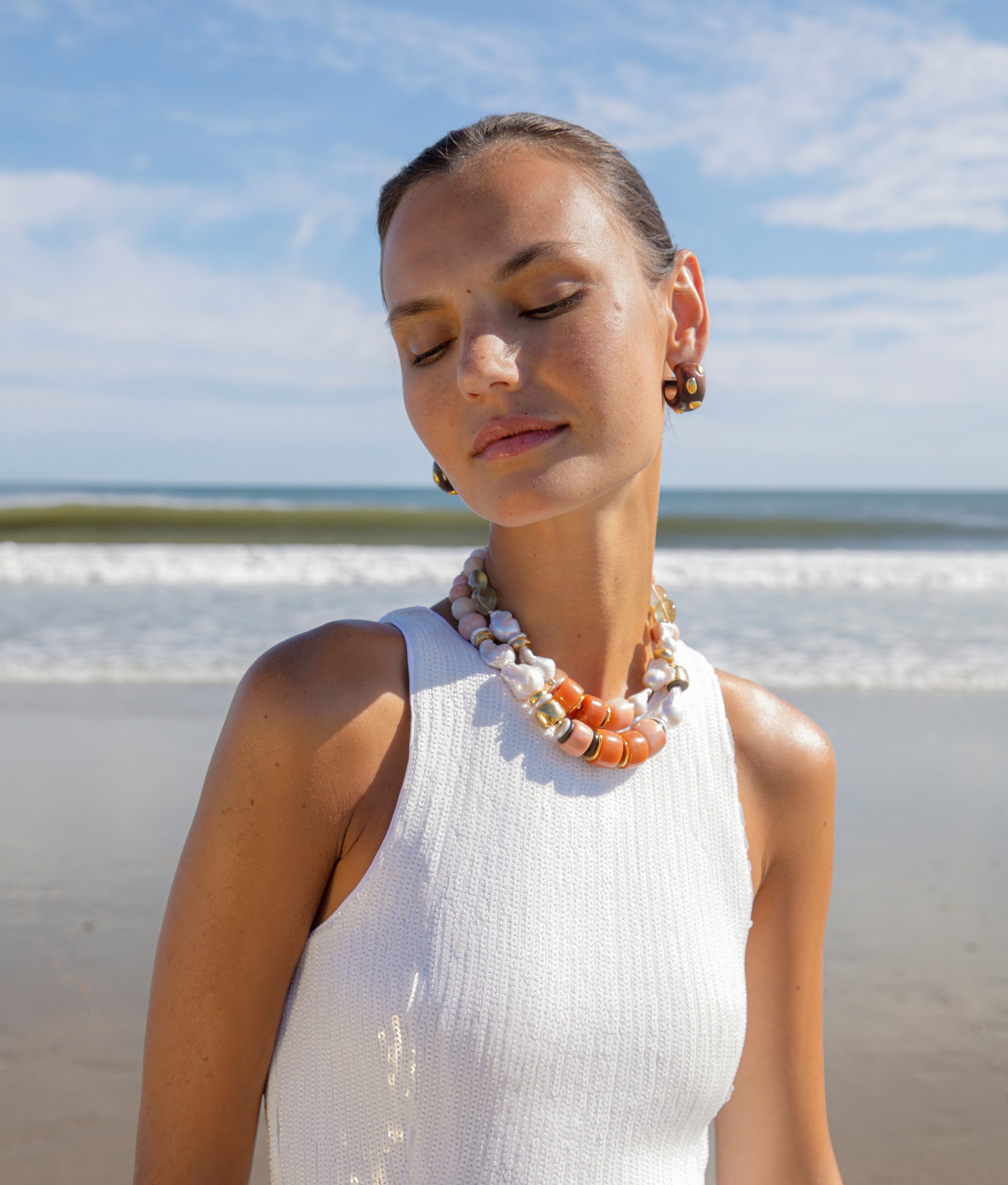 Model at the beach wearing Ariel II Necklace paired with Acacia Earrings in Gold Stud.