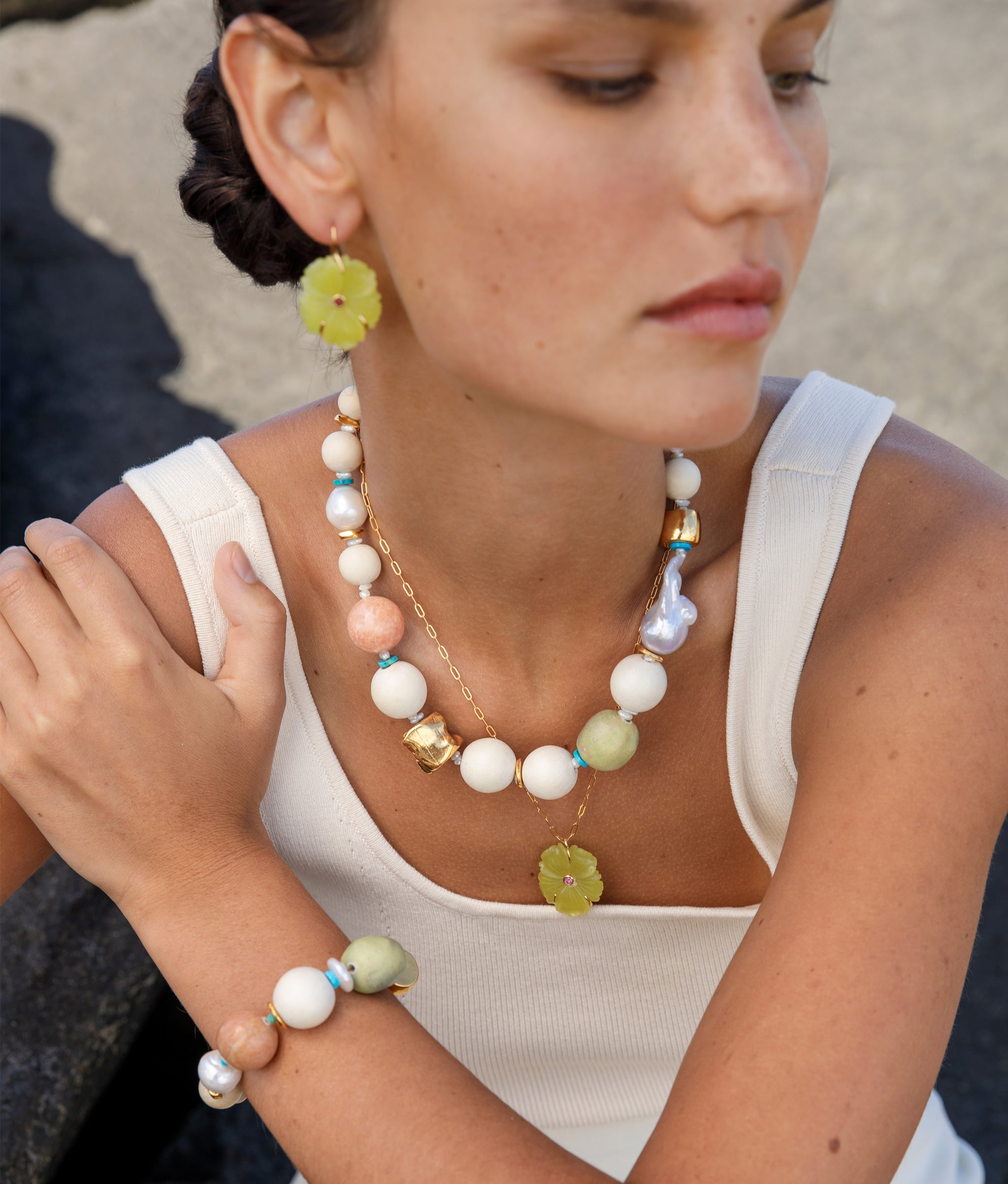 Closeup of model wearing Andros Bracelet and Necklace, paired with yellow-green floral necklace and earrings.