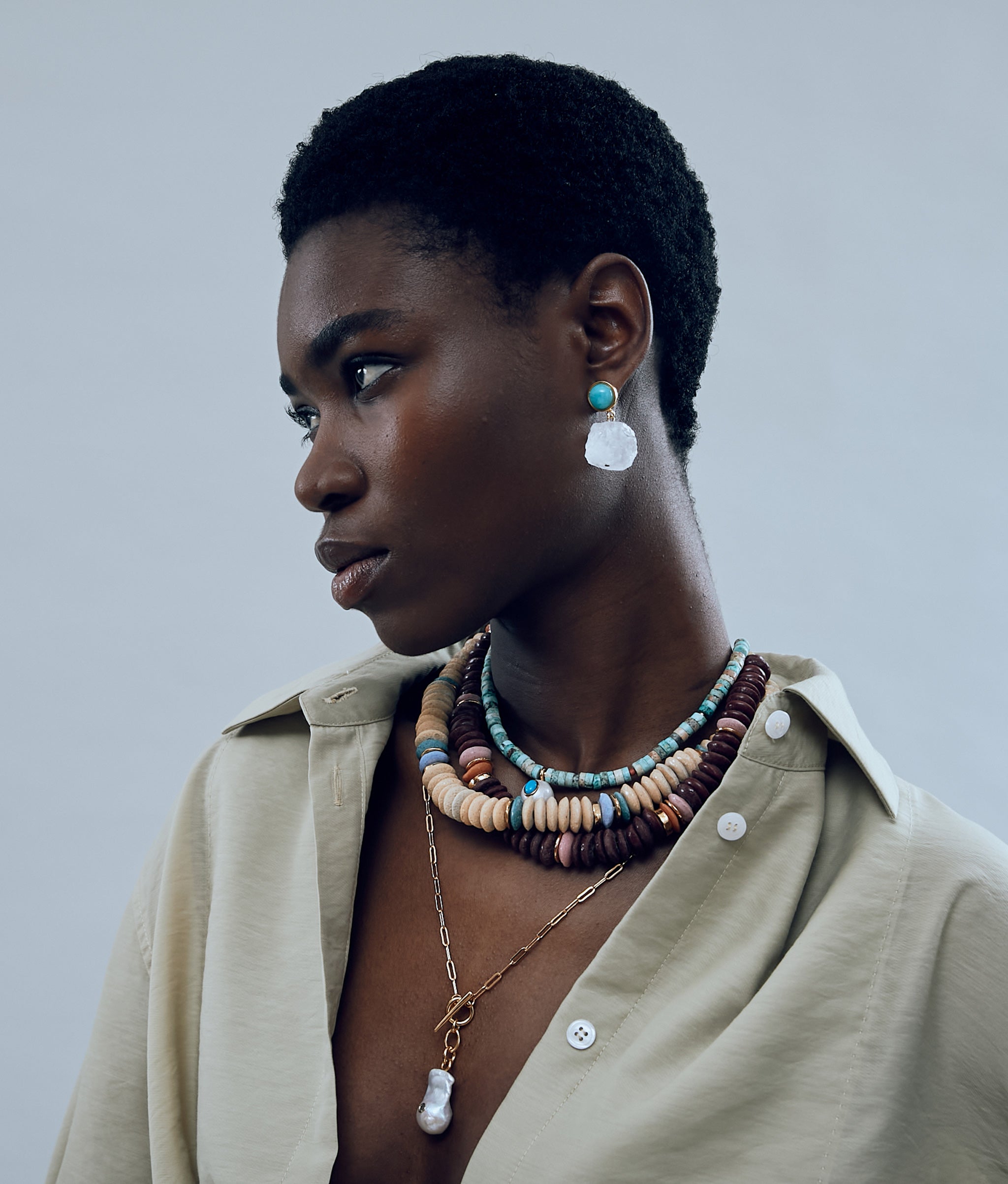 Model on grey background wearing the Glacier Bay Earrings in Rock Crystal with a myriad of colorful, chunky necklaces.