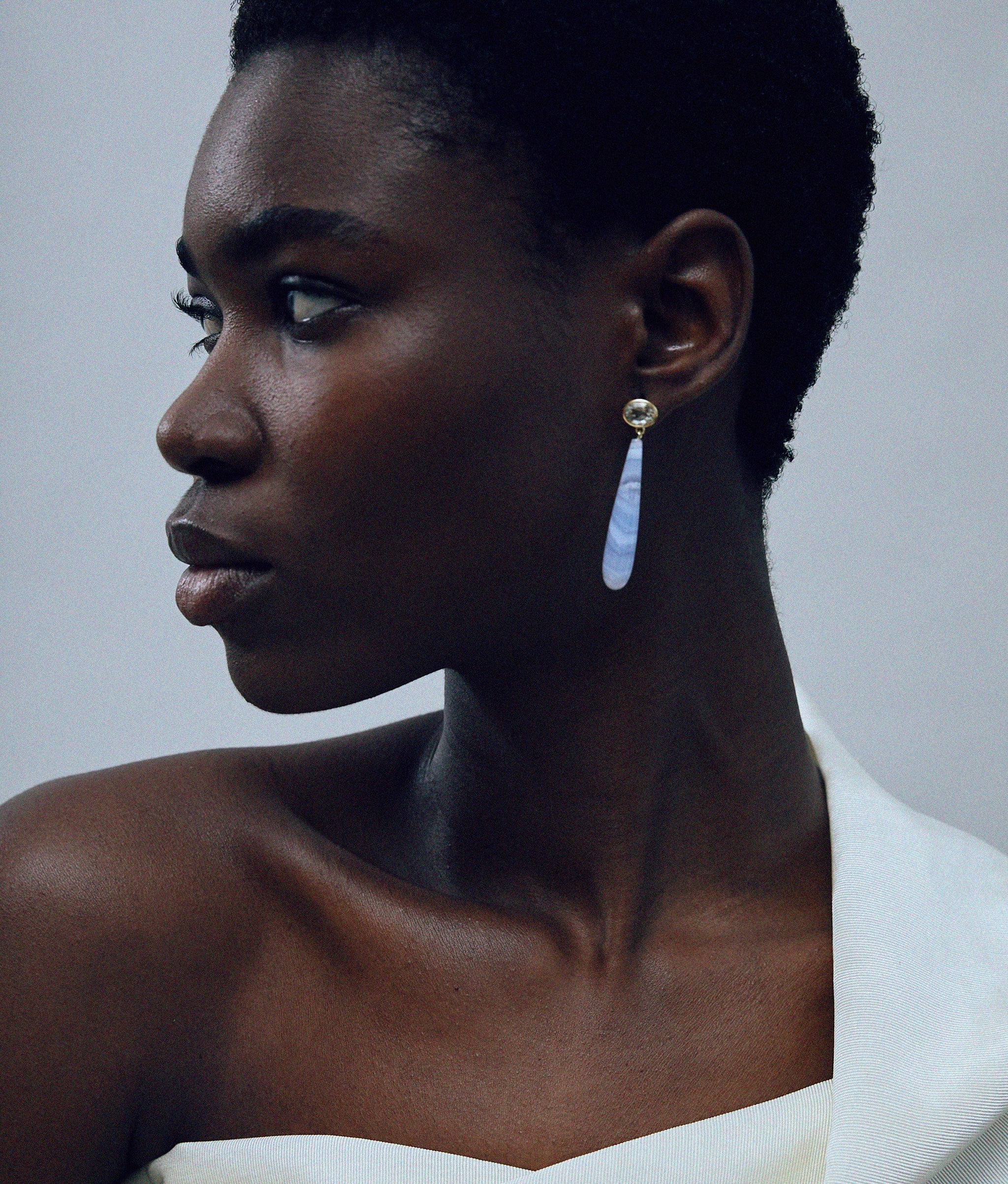 Close-up of model on grey background with 14k Gold Drop Earrings in Green Amethyst & Blue Lace Agate. 