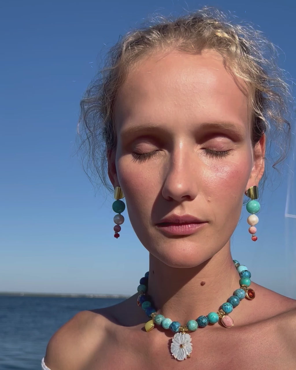 Video of model on blue sky wearing white off-shoulder top, Pego Earrings and Rockrose Necklace.