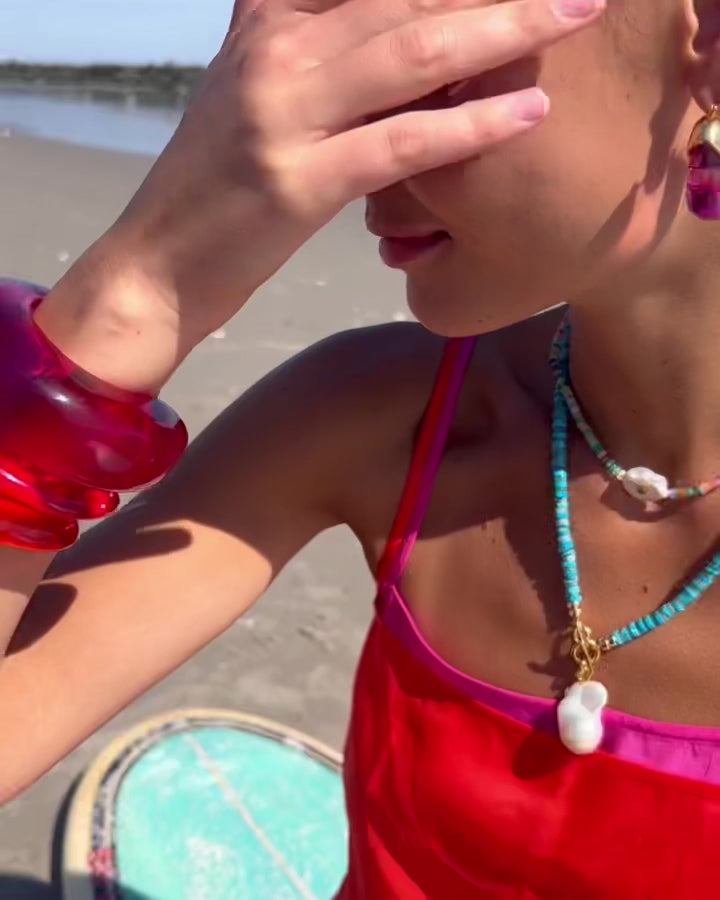 Video of model wearing Pearl Isle necklace paired with cuffs in Magenta and Persimmon and Organic Hoops in Flamingo.