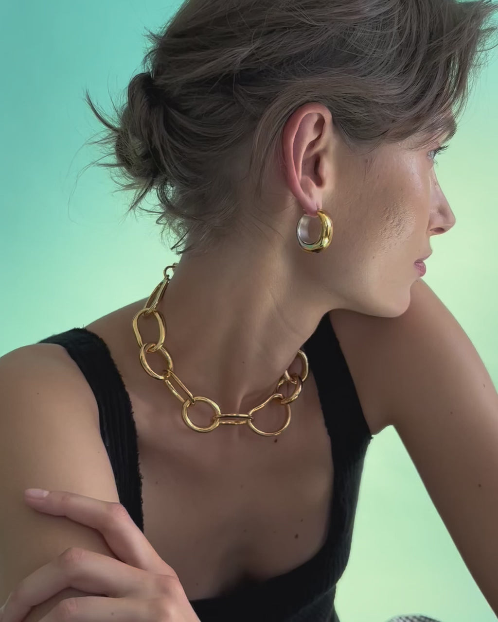 Video of model on blue backdrop, arms crossed and wearing black tank with Bubble Hoop Earrings and Porto Chain.