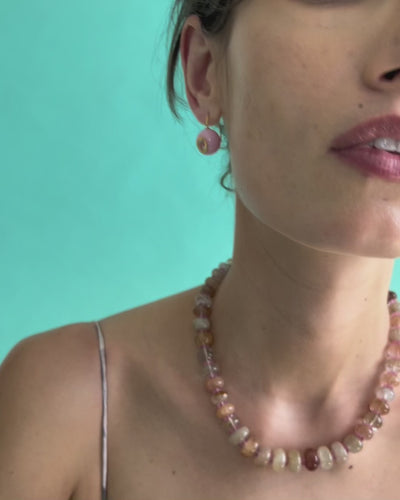 Close-up video of model on blue backdrop, in strappy dress with Pablo Earrings in Rose and Pink Cliffs Necklace.