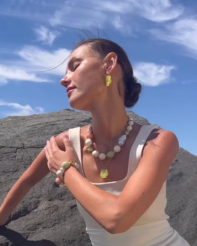 Video of model at the beach wearing Andros Bracelet and Necklace, paired with yellow-green floral necklace and earrings.