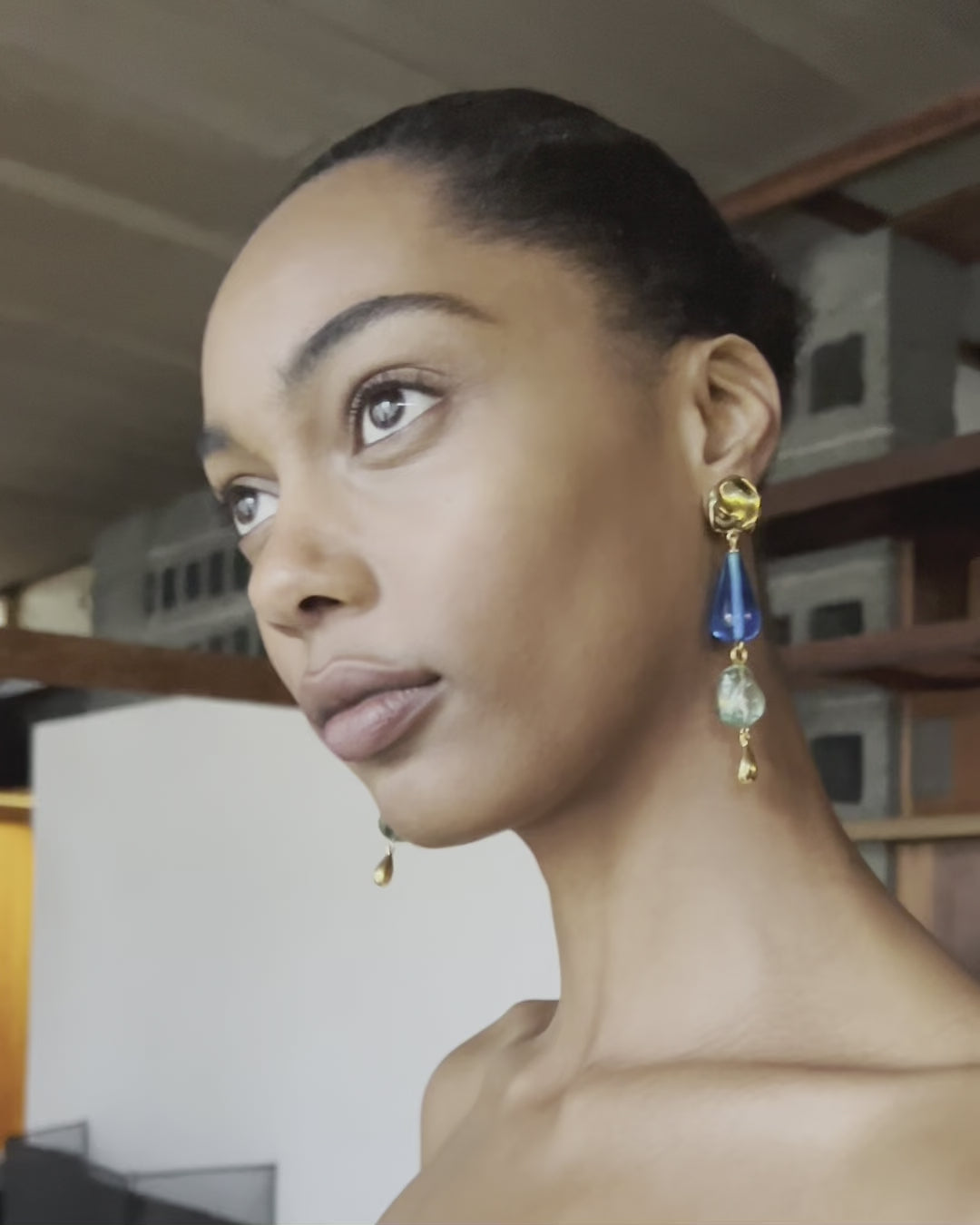 Video of model against wooden shelves, wearing Palma Earrings.