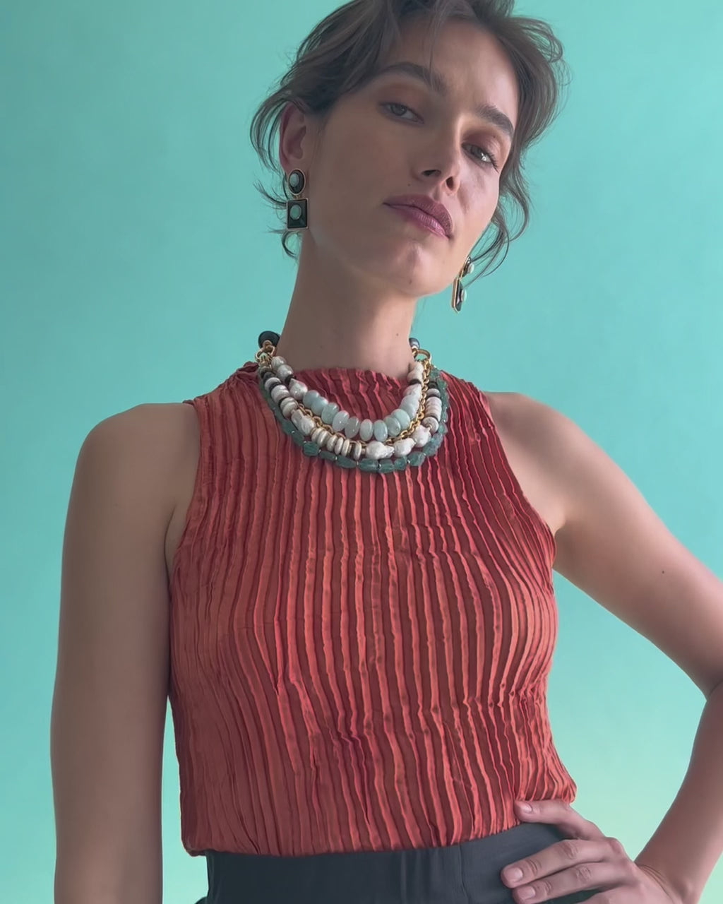  Video of model on blue backdrop, hands on hips, wearing orange top with Catalonia Necklace and Ethereal Pool Earrings.