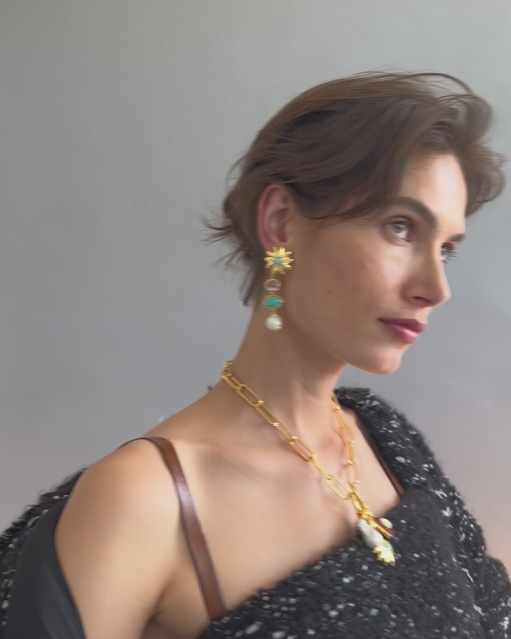 Video of model posing on grey backdrop in black textured outfit with Aphrodite Earrings and Helios Charm Necklace.