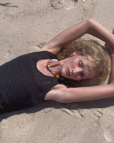 Video of model lying on sand, wearing black lace top with Concha Necklace and Marina Drop Earrings.