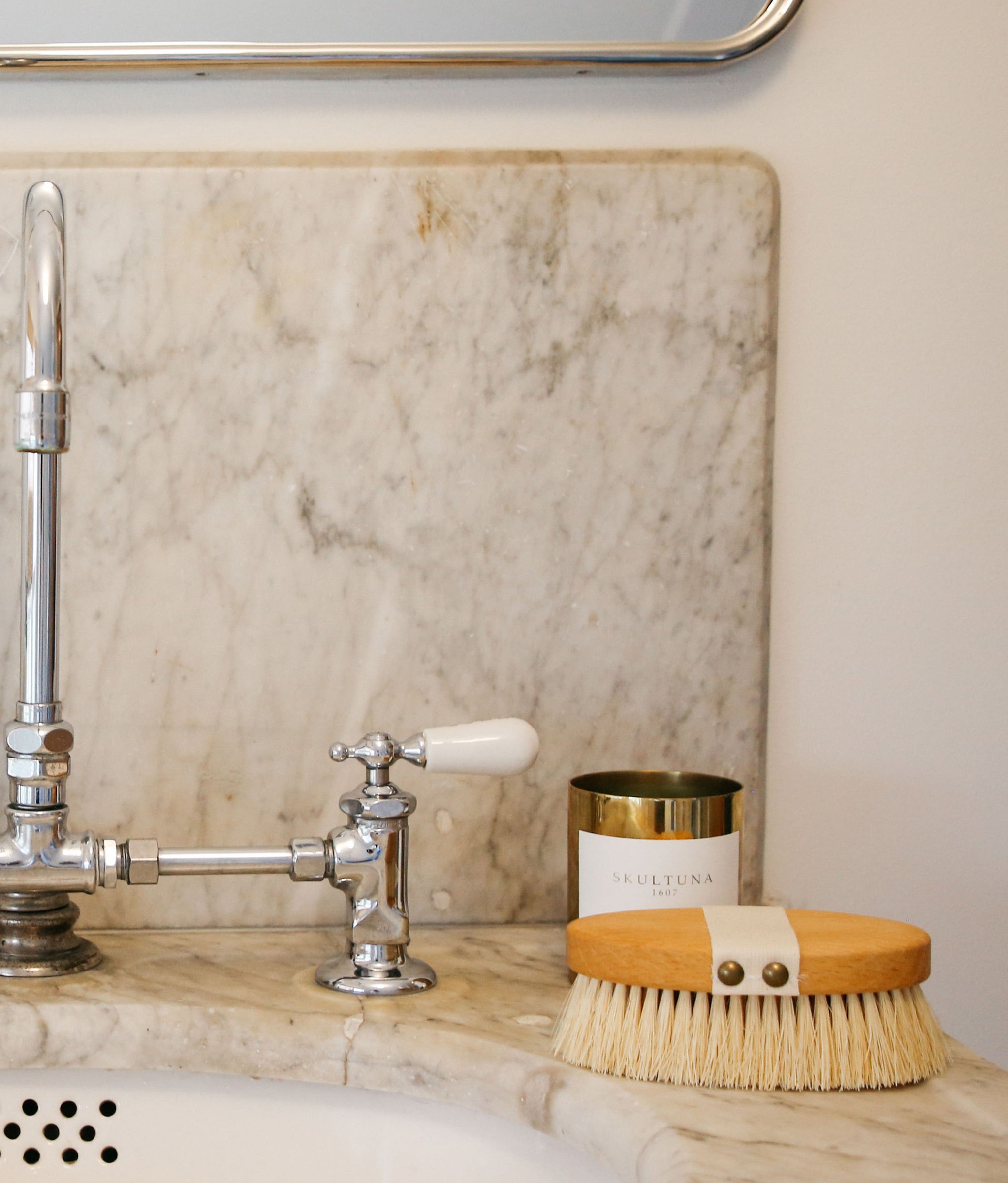 Massage Brush sits on marble sink with silver faucet and gold candle.