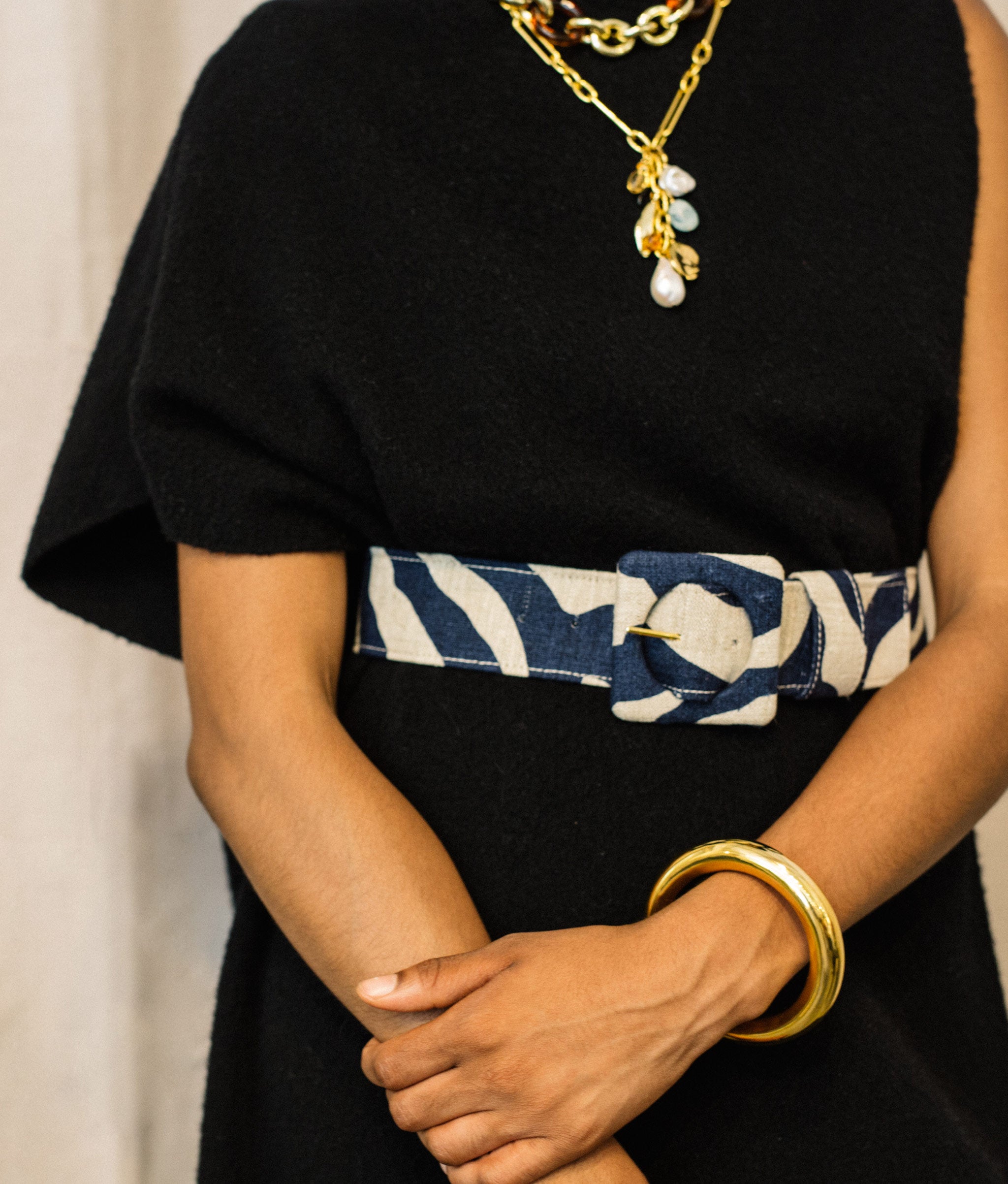 Model's torso in black sleeveless sweater dress with Agnes Belt in Indigo Zebra and assorted necklaces. 