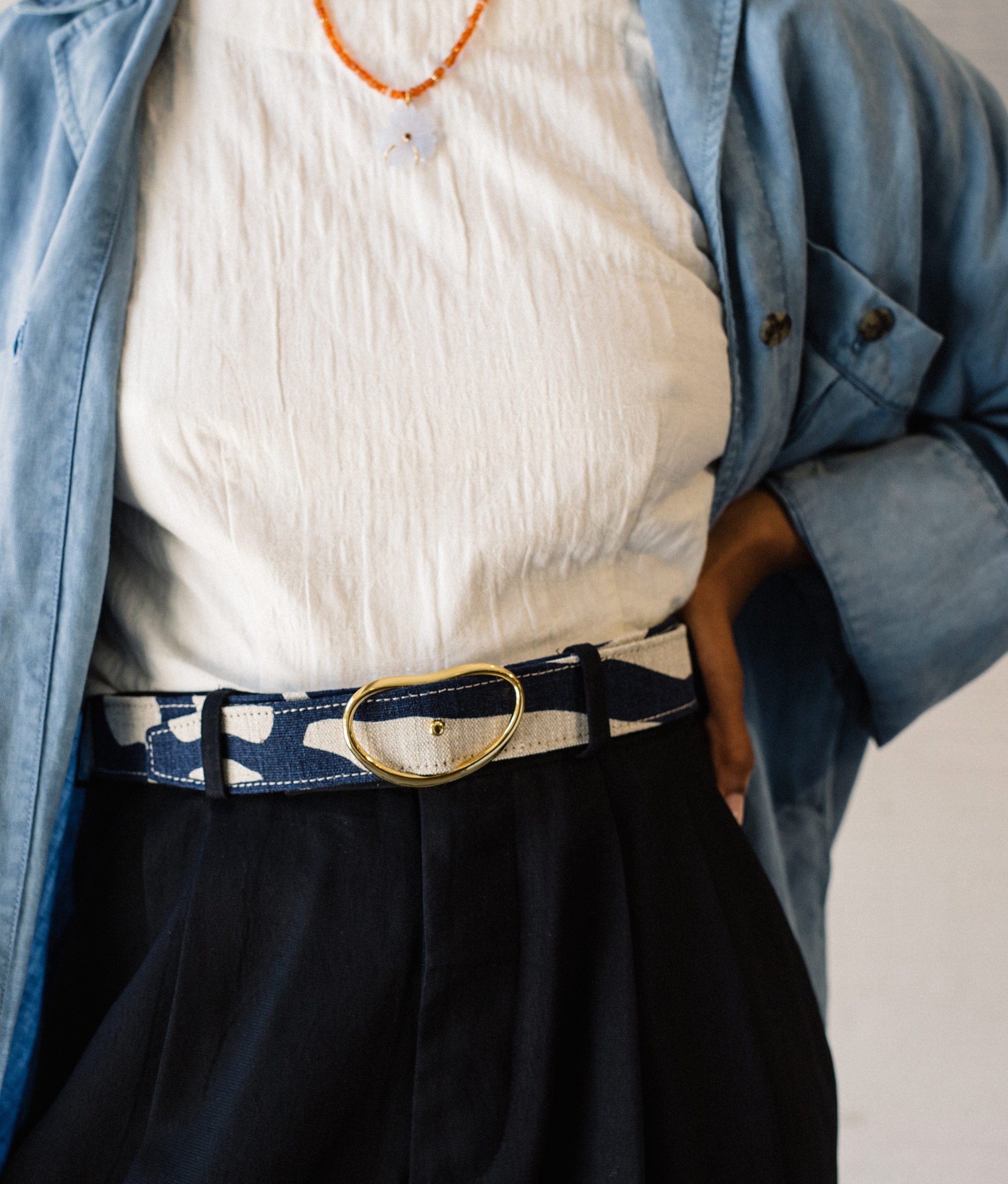 Model's torso in white top, chambray shirt and black pants,  with Wide Georgia Belt in Indigo Zebra and New Bloom Necklace.