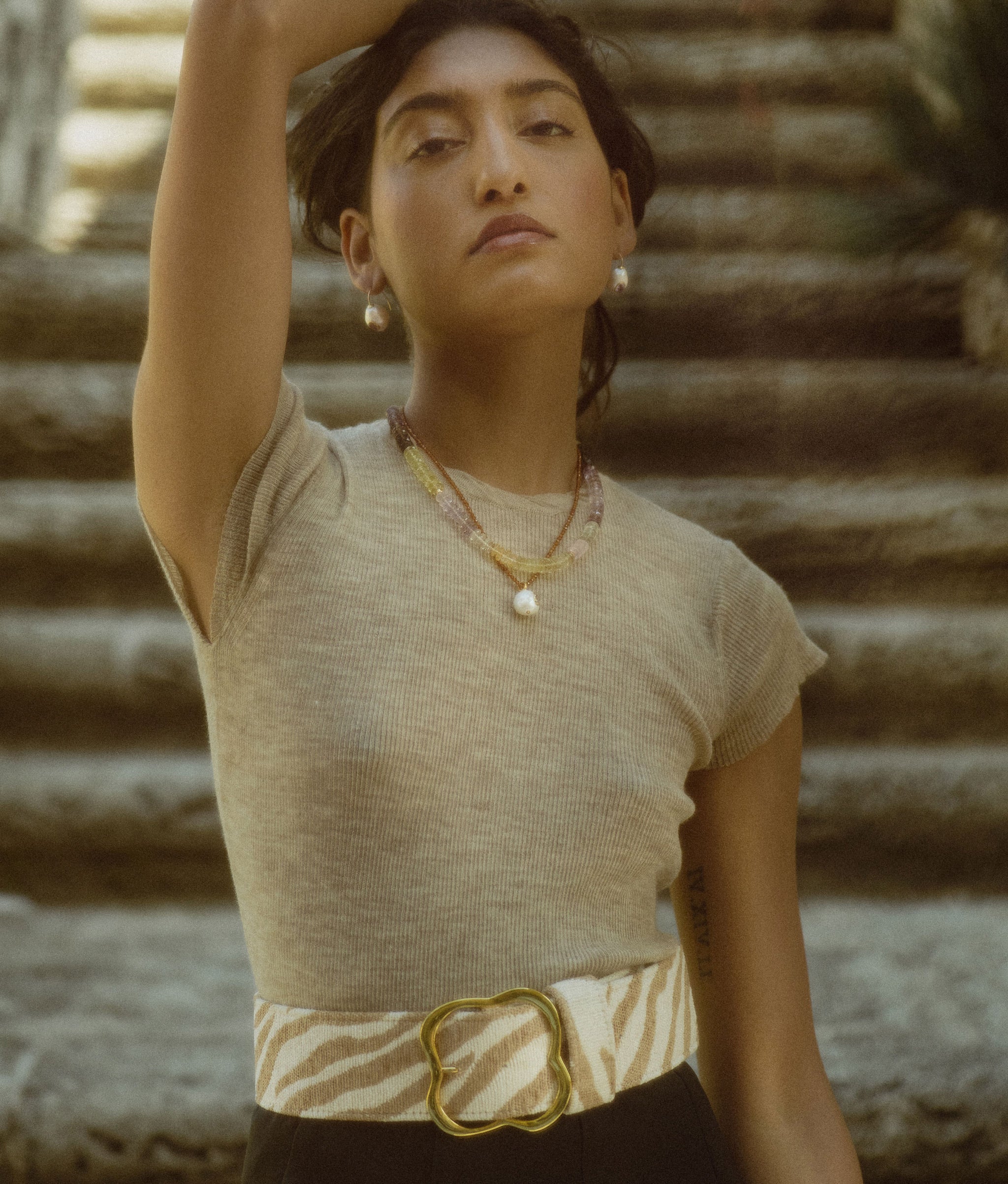 Model in front of stone steps wears beige tee with Castillo and Selena Necklaces, Pearl Pablo Earrings and Florence Belt.