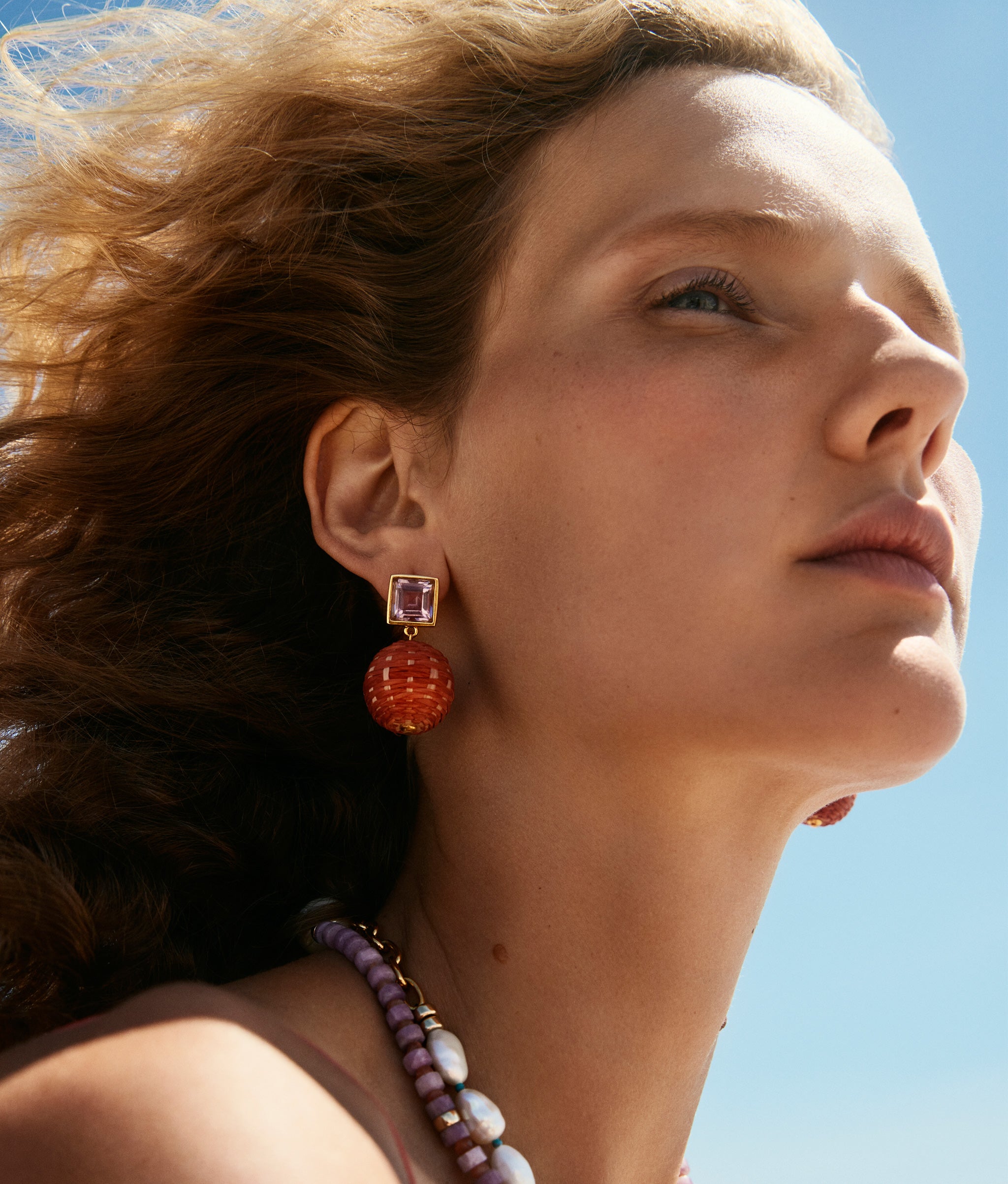 Model in profile wears Porto Covo Necklace and Paradiso Earrings in Terra Cotta.