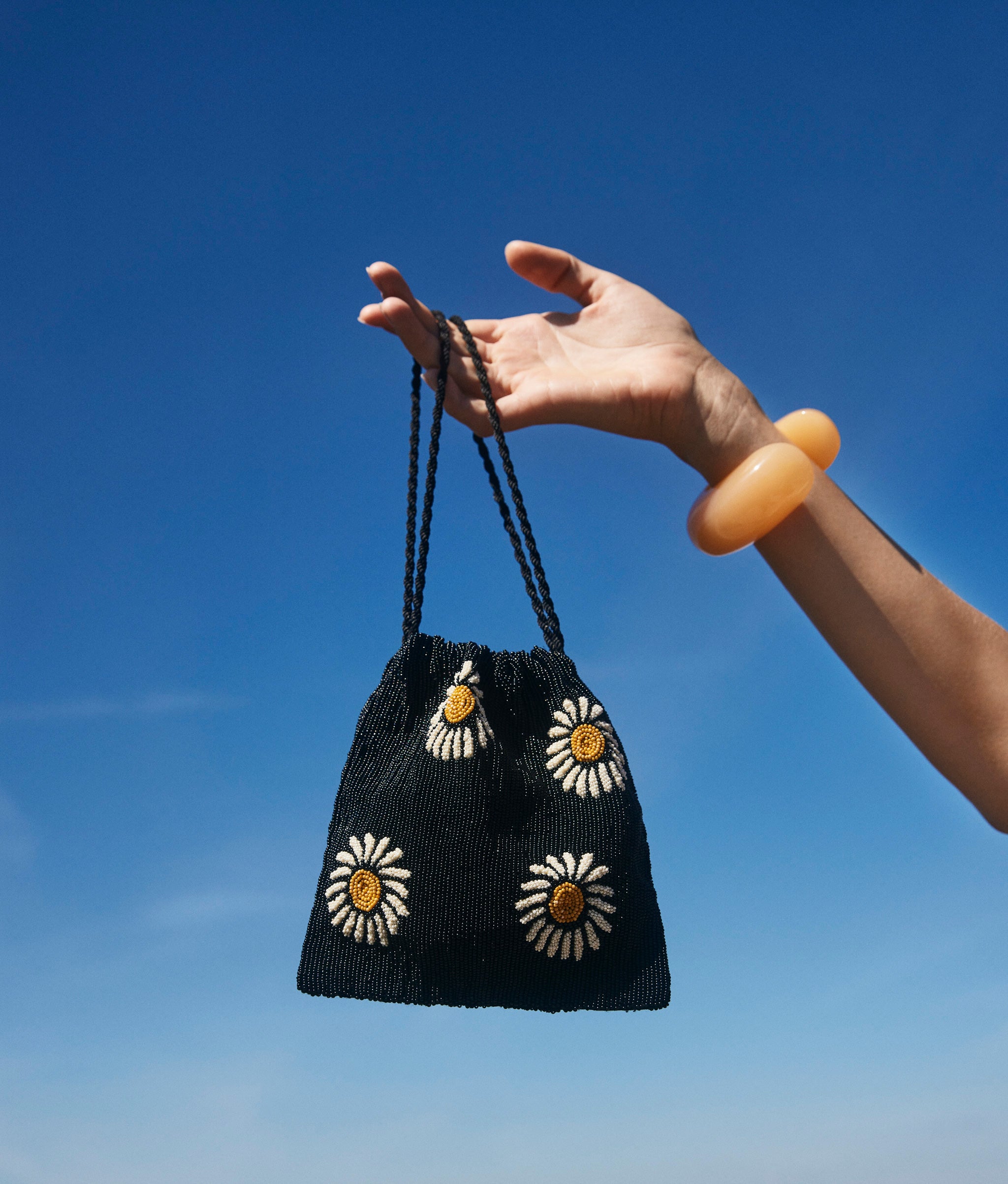 Hand holds up Gala Bag in Midnight Daisy against blue sky background.