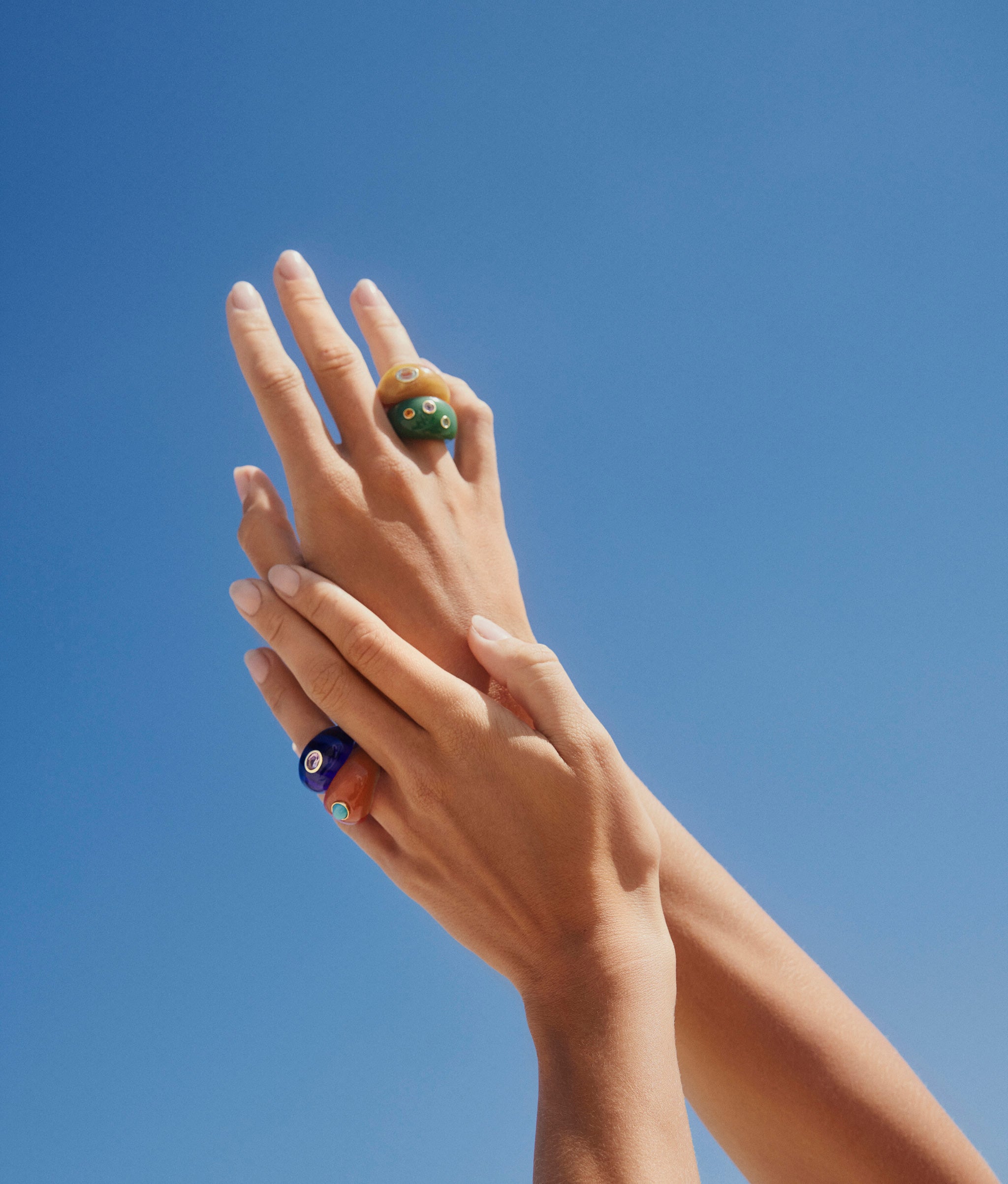 Model's hands up in sky wear Monument rings on both hands in Azure, Ochre, Jade and Terra.