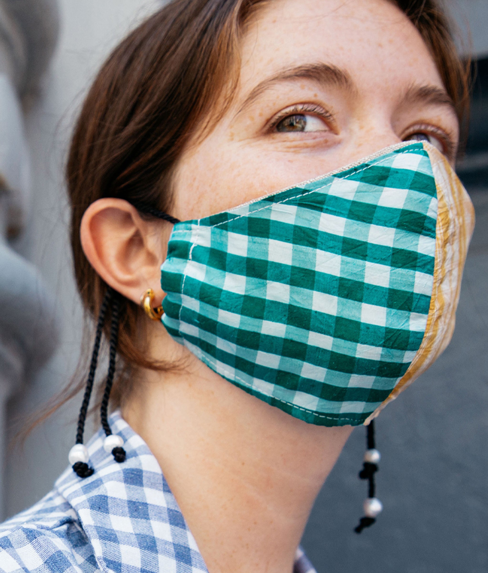 Model against grey wall and white column wears blue gingham shirt and Face Mask in Picnic.
