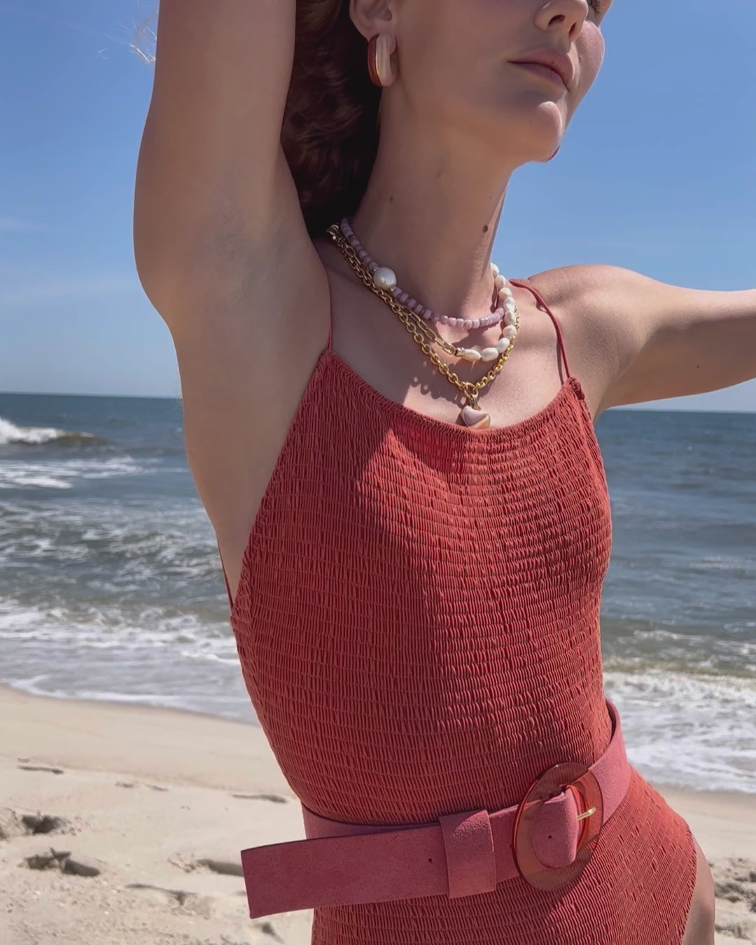 Video of model on beach in coral-colored swimsuit with Louise Belt in Conch Suede and assorted jewelry.