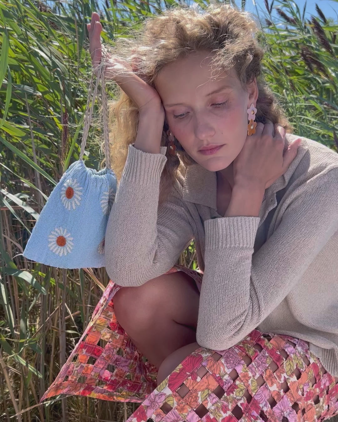 Video of model crouching in grass, wearing Camilo Drop Earrings and holding Gala Bag in Blue Daisy.